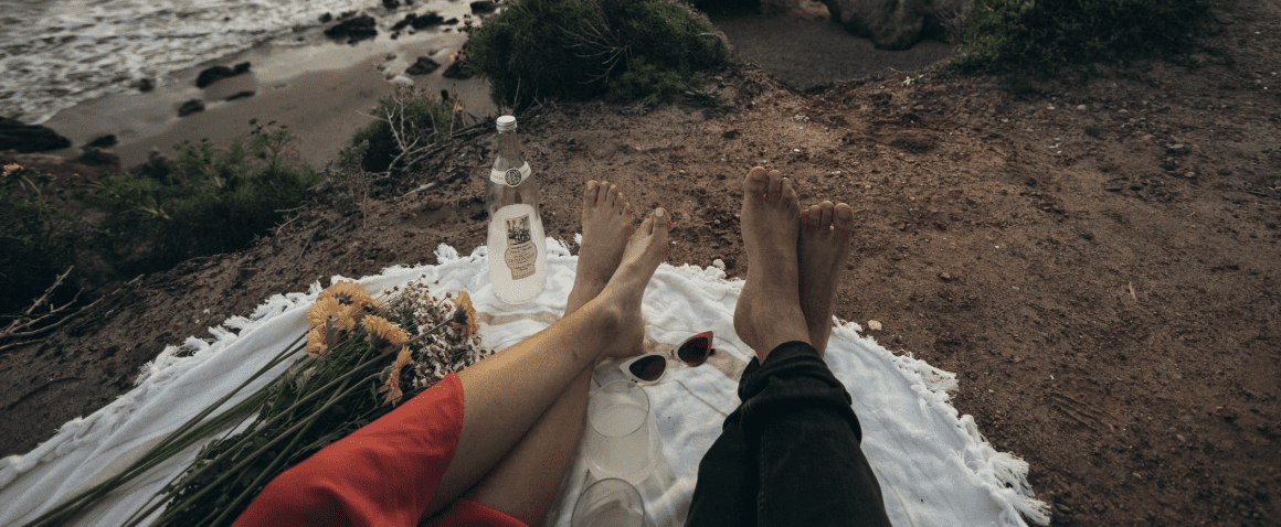 man-vrouw-voeten-zand-strand-picknick-bloemen-drank-romantisch